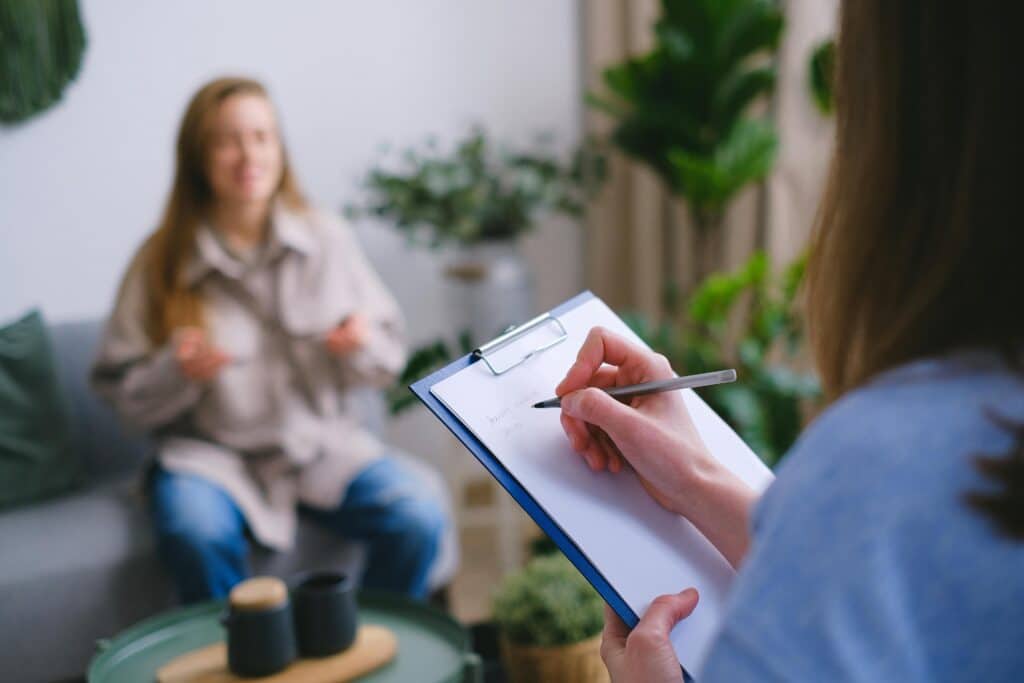 pexels photo 7176026 7176026 Unrecognizable professional female psychologist writing on clipboard while sitting against client on blurred background during psychotherapy session in light office